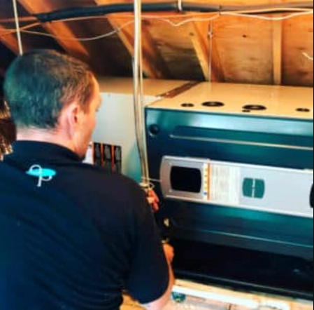 Technician servicing a furnace in an attic space.