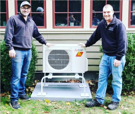 Two HVAC technicians standing beside a Mitsubishi air conditioning unit.