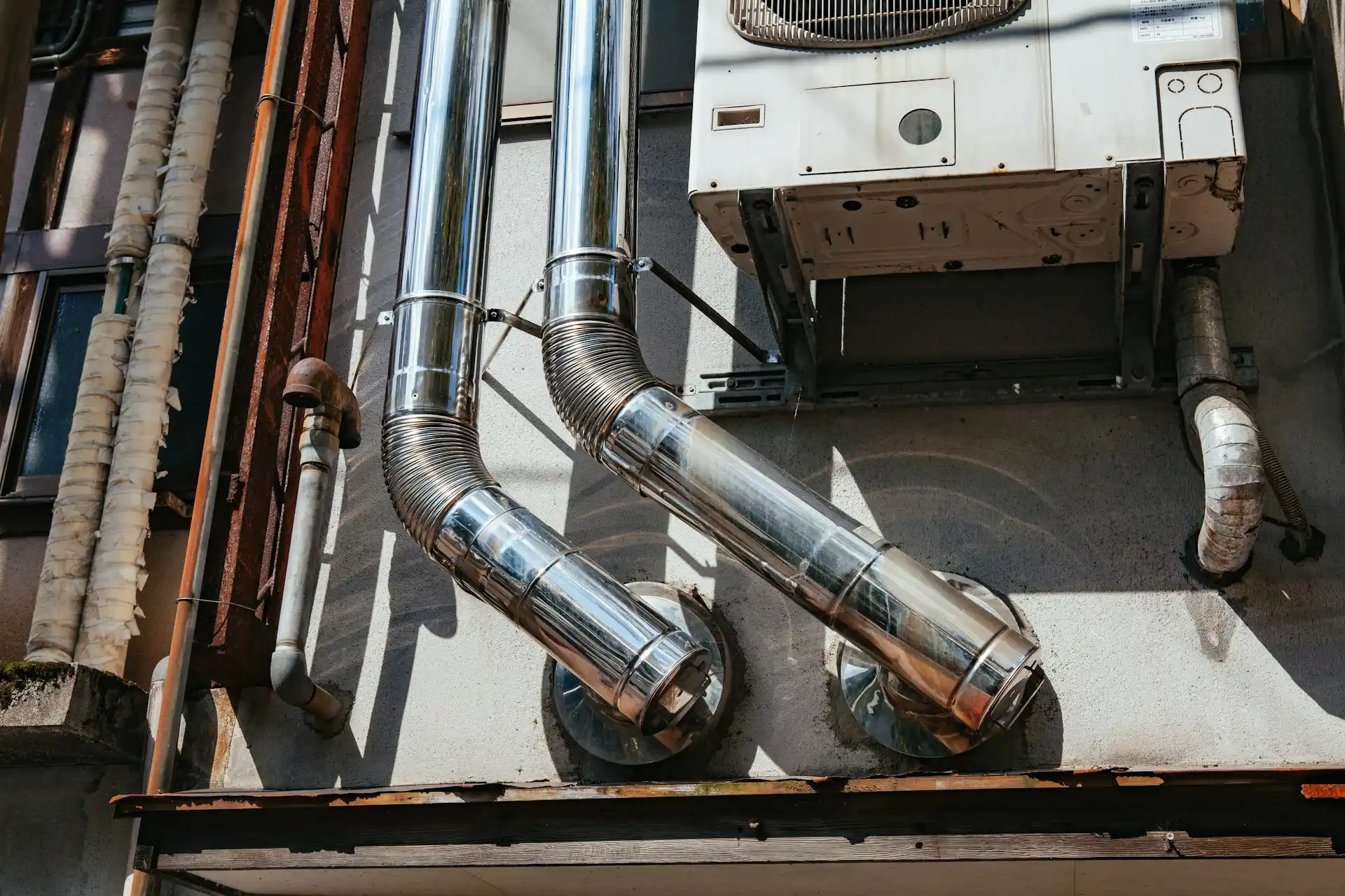 furnace-installation Metal exhaust pipes connected to an air conditioning unit on a building wall.