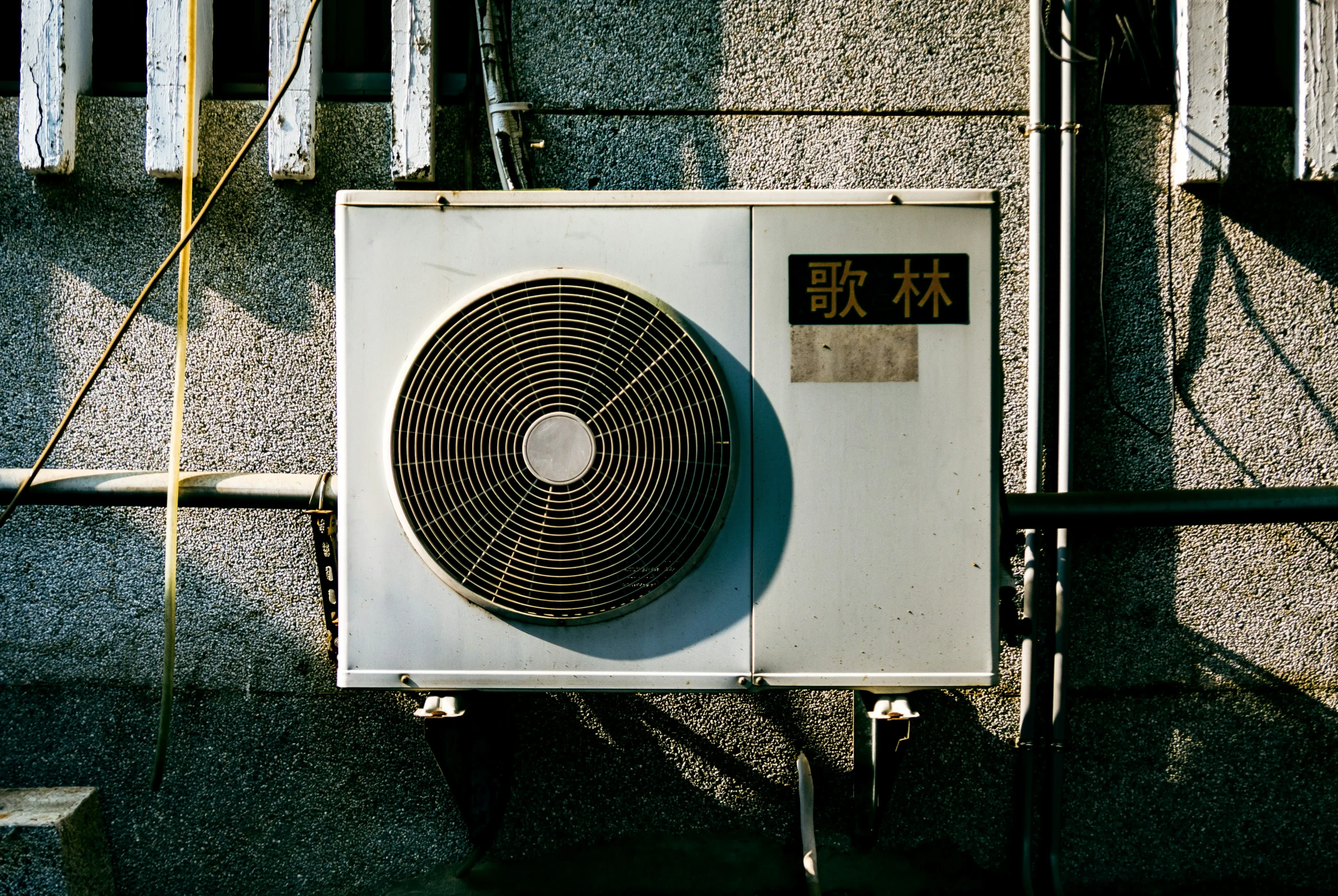 ticka-kao-1KNFO2dpoiM-unsplash Wall-mounted air conditioning unit with Chinese characters on a textured wall.
